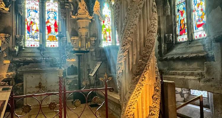 Intérieur de la Chapelle de Rosslyn présentant le Pilier de l'Apprenti richement sculpté et les vitraux colorés avec des rayons de lumière
