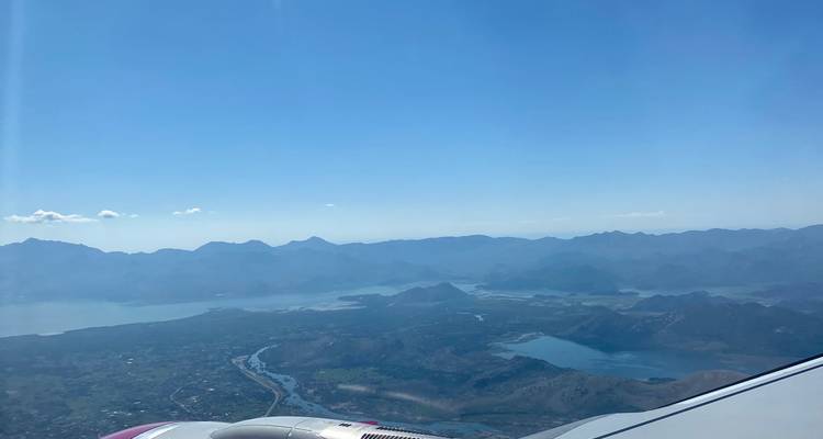 Vista aérea desde la ventanilla de un avión sobre montañas, valles y lagos en un día despejado