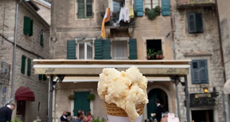 Cono de helado de vainilla sostenido frente a la fachada de un edificio de piedra rústica