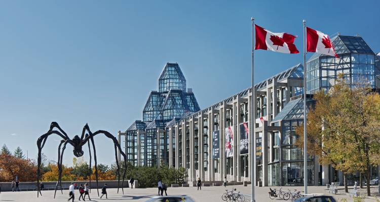 Complexe muséal d'art en verre moderne avec une gigantesque sculpture d'araignée noire et deux drapeaux canadiens flottant dans la plaza.