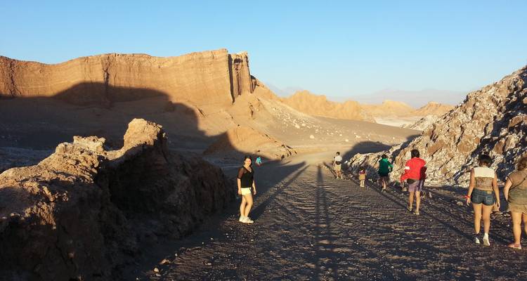 Les randonneurs marchent le long d'une route désertique poussiéreuse flanquée de falaises ocre imposantes à l'heure dorée.