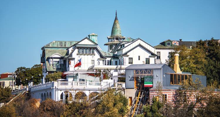 Demeure pittoresque perchée sur une colline avec une tour pointue dominant la ville côtière sous un ciel bleu dégagé.
