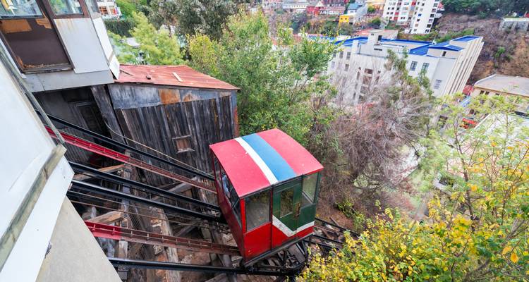 Un tramway funiculaire rouge vintage descend les voies raides de la colline parmi les arbres et les bâtiments colorés.