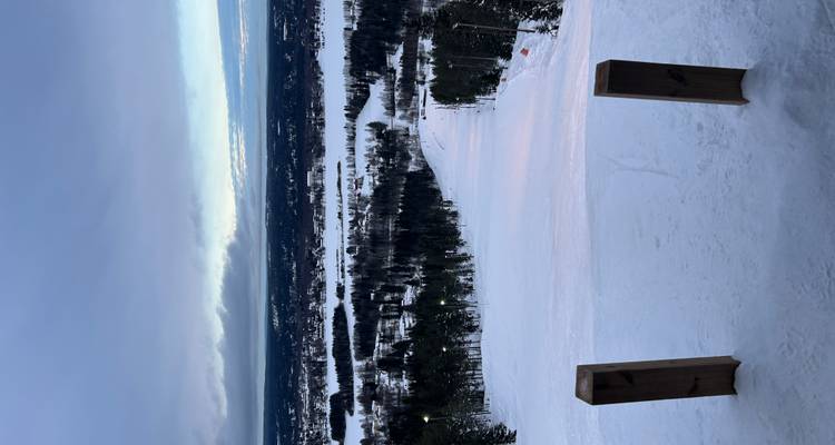 Vue depuis le sommet de la piste surplombant des lacs forestiers et une ville lointaine sous un ciel d'hiver menaçant.