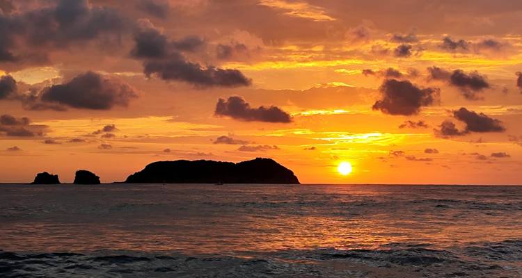 Briljant oranje zonsondergang achter een klein rotsachtig eilandje op een rustige zee.