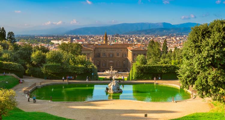 View over Palazzo Pitti and an emerald pond in the Boboli Gardens with Florence and mountains beyond.