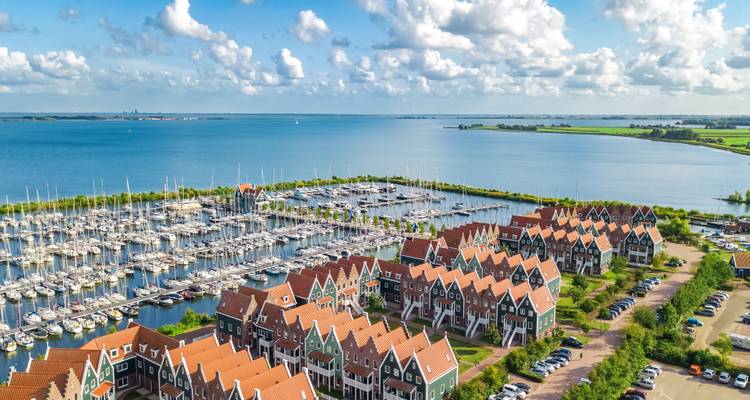 Vue aérienne de la marina de Volendam avec des rangées de maisons hollandaises aux toits rouges bordant un vaste lac bleu