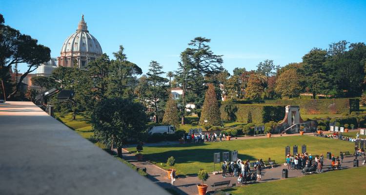 Vue panoramique sur les jardins du Vatican entretenus avec la coupole de la basilique Saint-Pierre dominant les visiteurs.