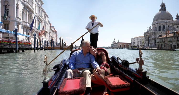 Gondolier manoeuvrant une gondole tandis qu'un couple s'enlace en glissant le long du Grand Canal de Venise à côté d'une église aux dômes