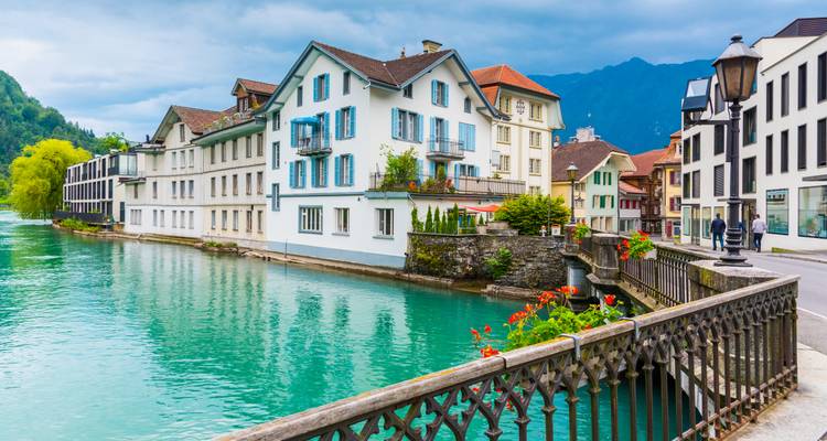 Charming riverside houses with teal water and mountain backdrop in Interlaken.