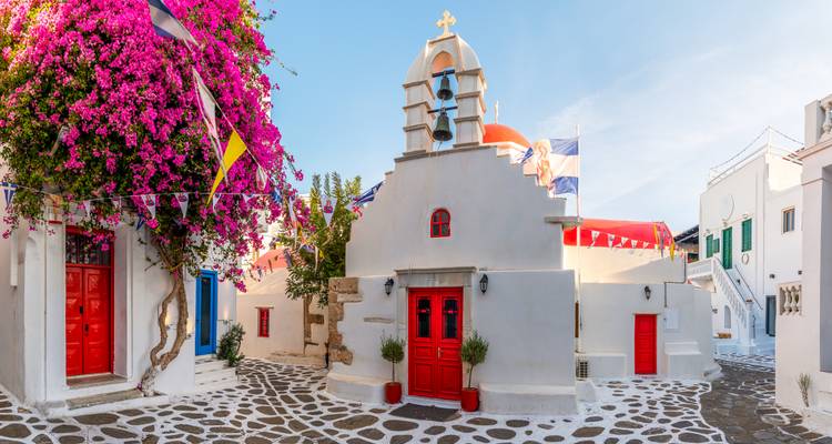Église cycladique blanchie à la chaux avec du bougainvillier vibrant et des portes rouge vif dans les ruelles labyrinthiques de Mykonos.