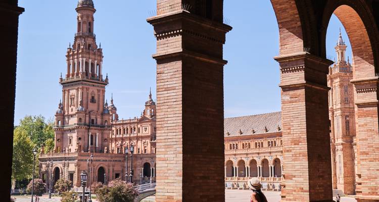 Voyageur admirant les arches et les tours de la Plaza de España de Séville encadrées par des colonnes en brique chaleureuse.