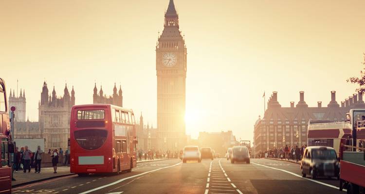 Le reflet du coucher de soleil derrière Big Ben tandis que des autobus rouges classiques et des voitures passent en flou sur le pont de Westminster.