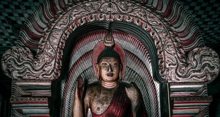 Statue de Bouddha peinte avec intricacité, encadrée par une arche ornée de temple troglodyte rouge et blanc.