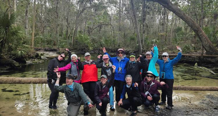 Groupe de randonneurs joyeux posant dans une forêt marécageuse à côté d'une source cristalline.