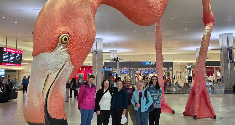 Groupe de voyageurs posant sous une gigantesque sculpture de flamant rose à l'intérieur d'un terminal d'aéroport.