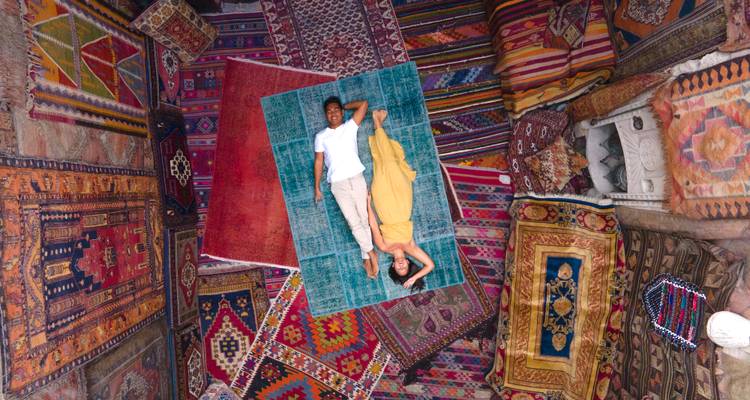 Vue de dessus d'un couple allongé sur un patchwork vibrant de tapis turcs traditionnels à l'intérieur d'une boutique de tapis colorée.