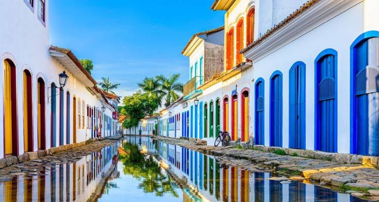 Kleurrijke koloniale straat in Paraty met levendige deuren weerspiegeld in regenvulde kasseien, fiets rustend tegen een muur.