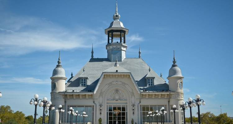 Elegant Frans-stijl museumgebouw met een sierlijk dak, centrale lantarentoren en rijen decoratieve lantaarnpalen onder een strakblauwe hemel