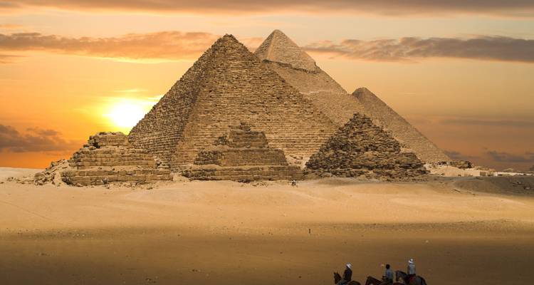 Grote Piramides van Giza afgetekend tegen een gouden zonsondergang met kleine kameerijders op de voorgrond