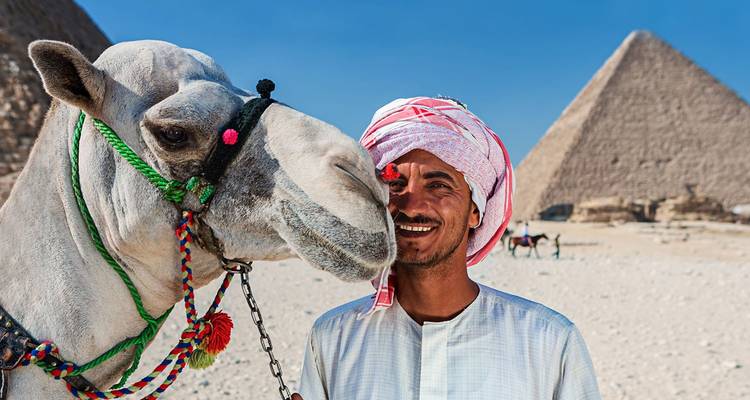 Ein lächelnder Kameltreiber posiert mit seinem geschmückten Kamel vor den Pyramiden von Giza.