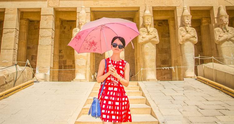 Ein Tourist mit einem rosa Regenschirm steht vor den kolossalen Statuen des Hatschepsut-Tempels in Luxor.