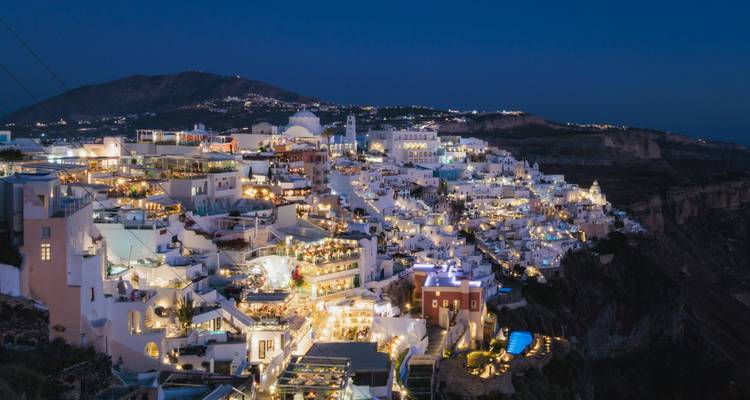 Avondpanorama van verlichte clifftop-dorpjes van Santorini die naar beneden storten naar de caldera in de schemering