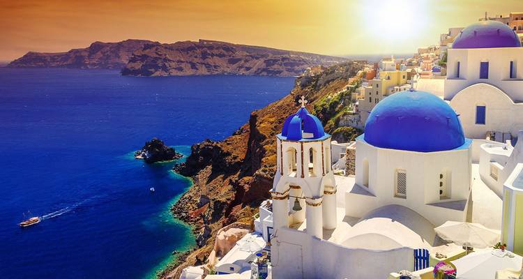 Gouden zonsondergang boven Santorini's blauwe koepels en rotsachtige caldera met de door zonlicht beschenen zee op de achtergrond