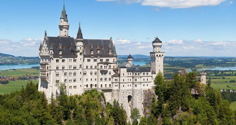 Le château emblématique de Neuschwanstein qui s'élève au-dessus de falaises boisées avec des lacs et des champs au-delà
