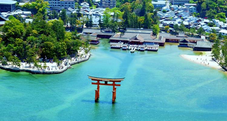 Iconisch rood torii-poortje dat in blauw water staat vlakbij heiligdomgebouwen en een bosrijke oever