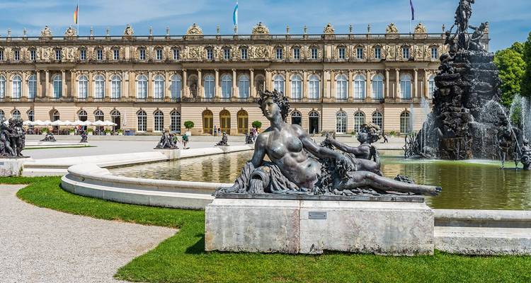 Estatua junto a una fuente ornamentada frente al Palacio de Herrenchiemsee en un día soleado