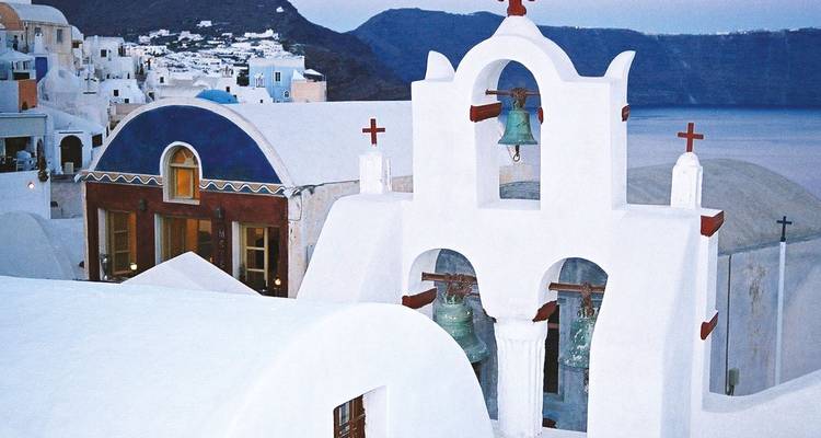 Witgekalkte Santorini kerkklokketoren met calderarotsen bij schemering.