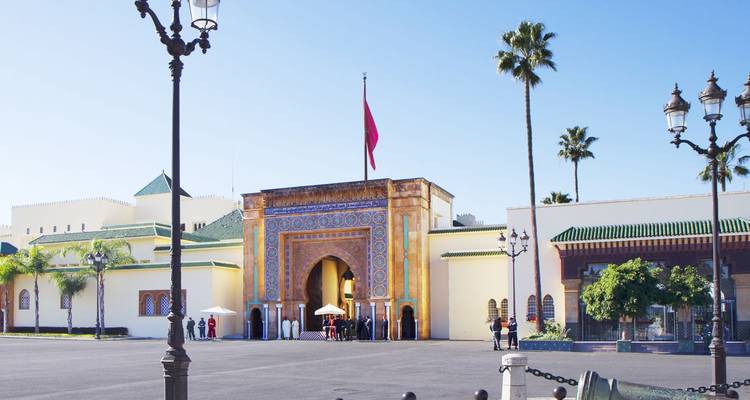 Elegant betegelde poort van het Koninklijk Paleis-complex die uitkomt op een ruim plein met een Marokkaanse vlag bovenop.
