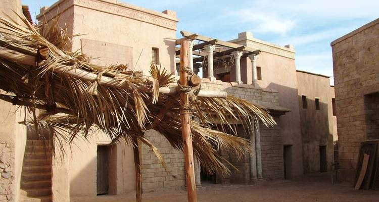 Adobe-gekleurde kasbah-gebouwen en ruwe palmtakendaken roepen een oud woestijndorp op.