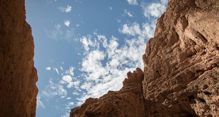 Steile rode rotswanden van de canyon omlijsten een stukje blauwe lucht met wat lichte wolkjes.