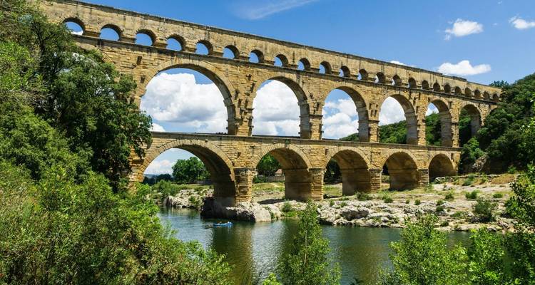 De oude stenen bogen van de Pont du Gard strekken zich uit over een rustige rivier omringd door weelderig groen.