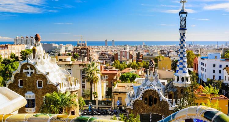 Kleurrijke mozaïeken terrassen van Park Güell kijken uit over de skyline van Barcelona en de verre zee.