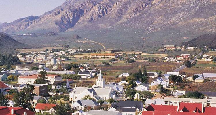 Pequeño pueblo rural con una iglesia blanca situada al pie de unas montañas marrones y escarpadas.