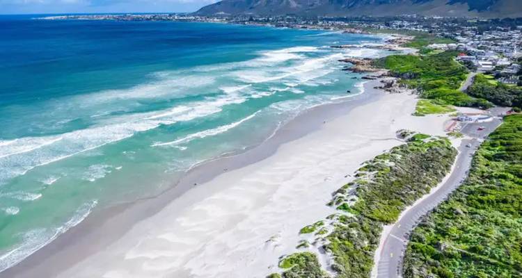 Amplia bahía de arena con olas rodantes y pueblo costero respaldado por montañas.