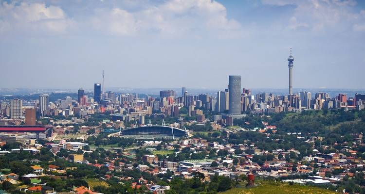 Skyline de Johannesburgo bajo cielos parcialmente nublados visto desde una colina lejana.