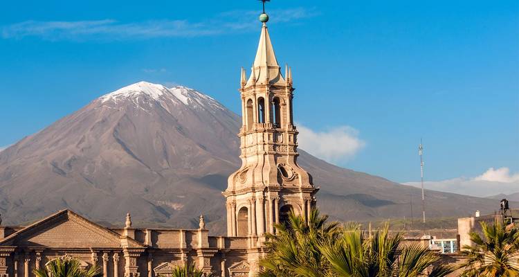 De met sneeuw bedekte El Misti-vulkaan rijst op achter de sierlijke toren van Arequipa's basilica onder een kristalhelder blauwe lucht.