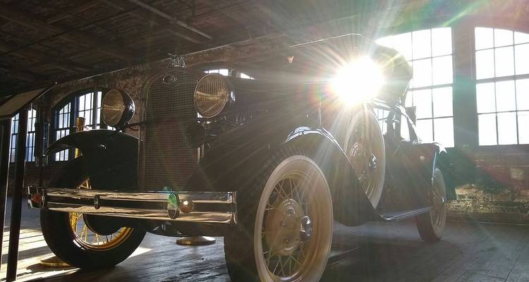 Automóvil vintage exhibido en interiores con luz solar dramática entrando por las ventanas del almacén.