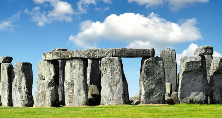 Ikonischer prähistorischer Steinkreis von Stonehenge, der auf einer offenen Grasfläche unter blauem Himmel steht