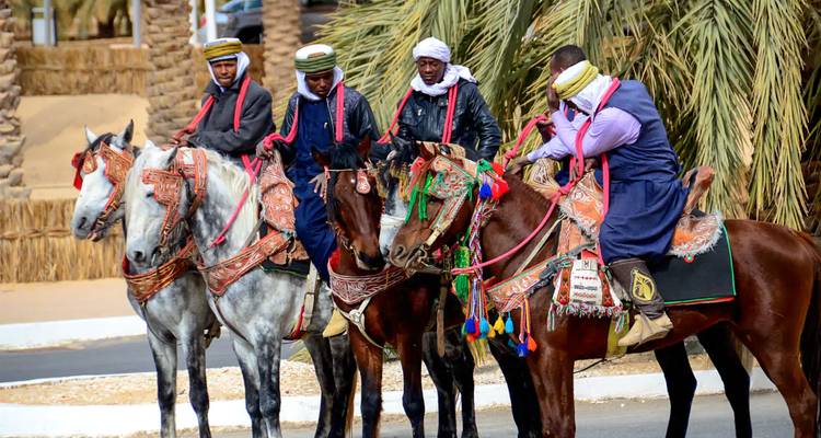 Traditionelle Reiter in farbenfroher Kleidung, die neben Palmen während eines Kulturevents in Algerien warten
