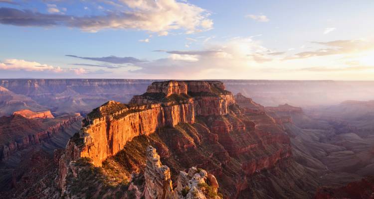 Sunset light bathes sheer cliffs of the Grand Canyon with layered ridges fading into mist.