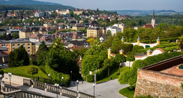 Erhöhte Aussicht über eine malerische europäische Stadt, umgeben von üppigem Grün und einem Flusstal.