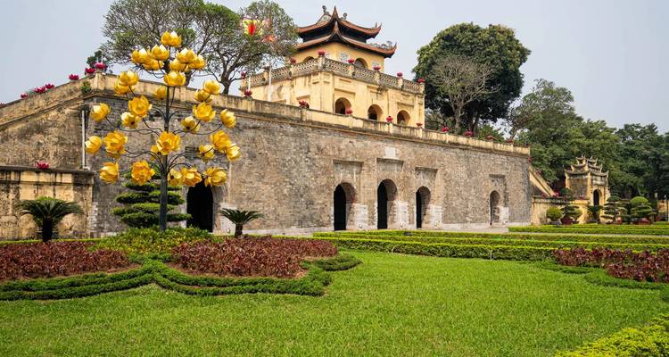 Ancient stone gate of the Imperial Citadel of Thang Long framed by manicured gardens and a decorative tree.