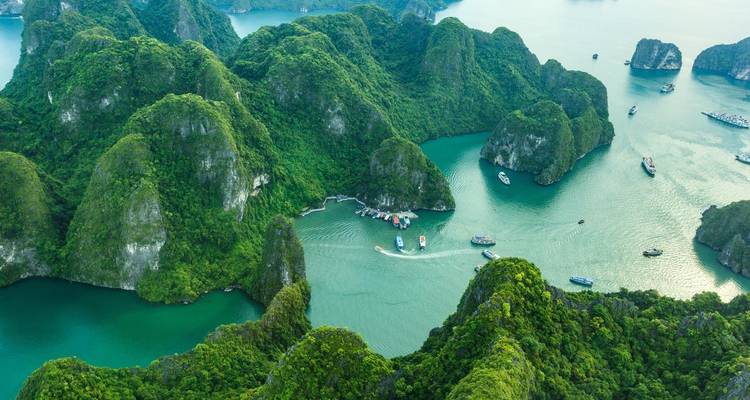 Aerial panorama shows lush green limestone islands rising from turquoise bays in Halong Bay.
