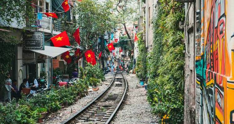 Railway track runs between narrow residential buildings adorned with Vietnamese flags in Hanoi Train Street.
