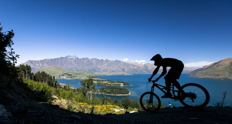 Silhouette d'un cycliste de montagne qui descend vers un lac turquoise et des pics alpins près de Queenstown.